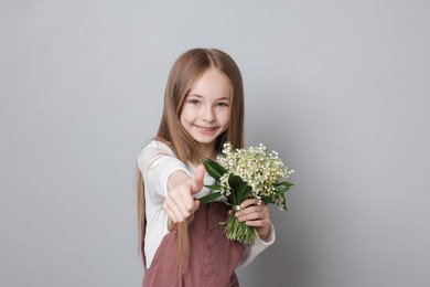 Photo of Girl with bouquet of beautiful lily-of-the-valley flowers showing thumbs up on light grey background