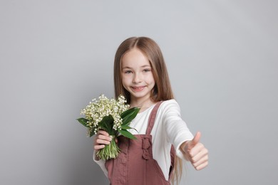 Photo of Girl with bouquet of beautiful lily-of-the-valley flowers showing thumbs up on light grey background