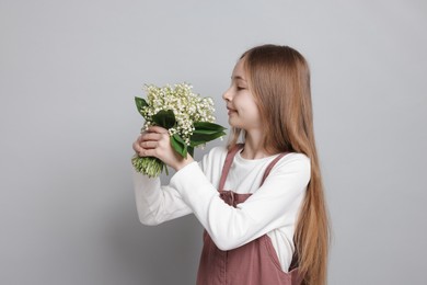 Photo of Girl with bouquet of beautiful lily-of-the-valley flowers on light grey background