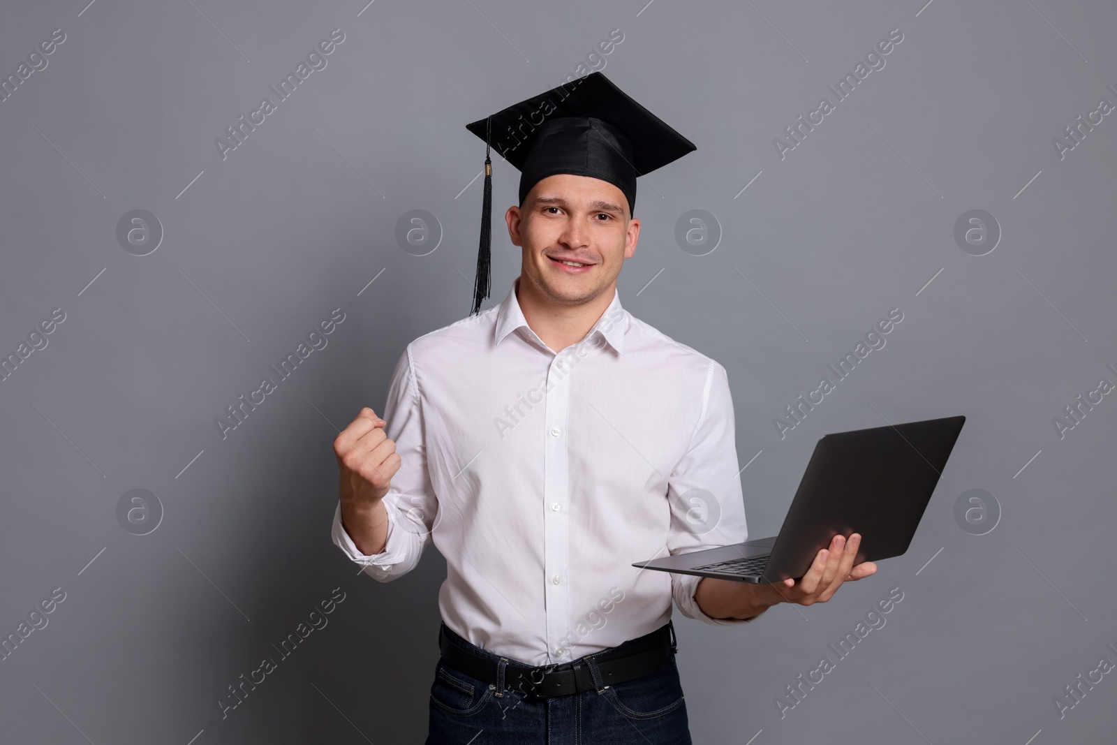 Happy student with laptop after graduation on grey background Photo of Happy student with laptop after graduation on grey background