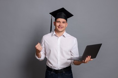 Photo of Happy student with laptop after graduation on grey background