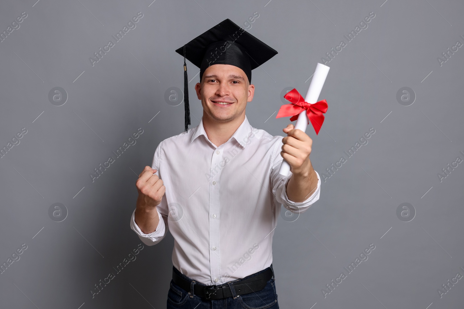 Happy student with diploma after graduation on grey background Photo of Happy student with diploma after graduation on grey background