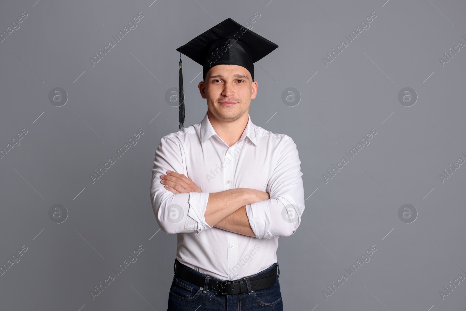 Student with crossed arms after graduation on grey background Photo of Student with crossed arms after graduation on grey background