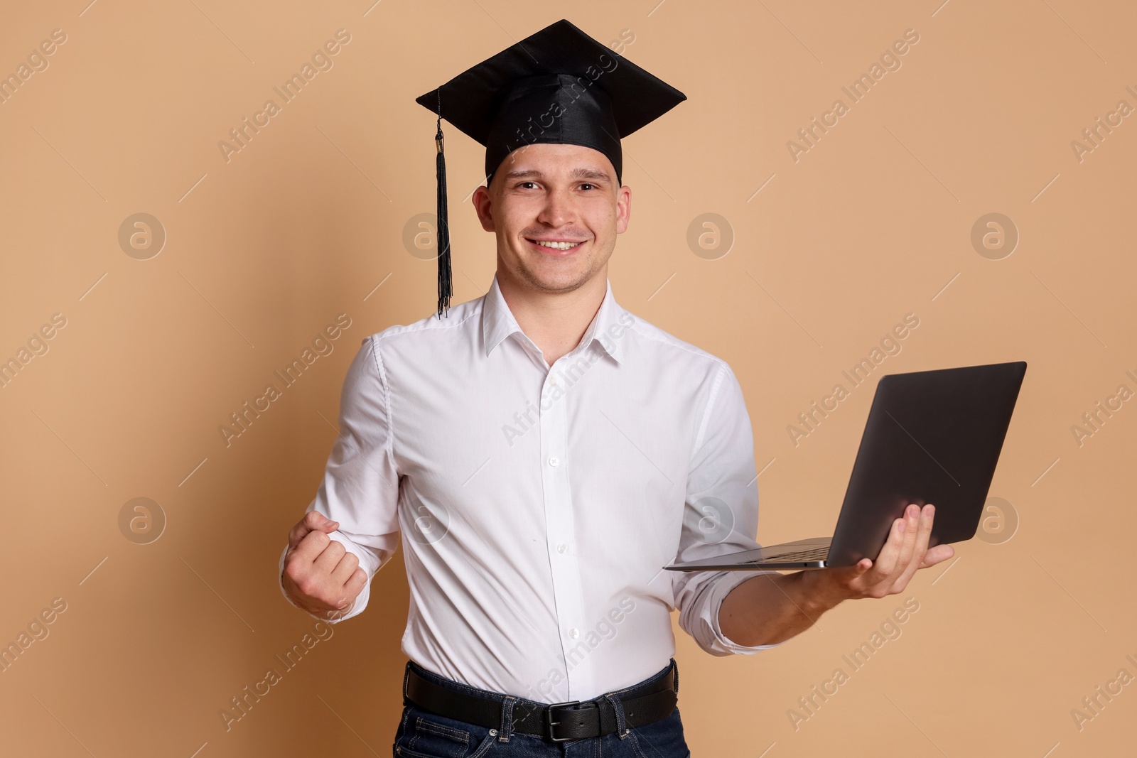 Happy student with laptop after graduation on beige background Photo of Happy student with laptop after graduation on beige background