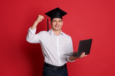 Photo of Happy student with laptop after graduation on red background