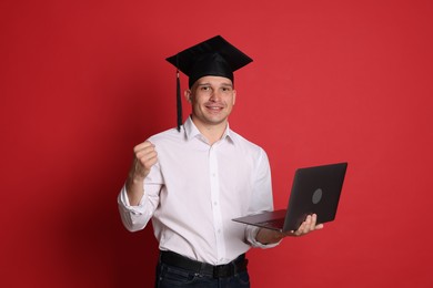 Photo of Happy student with laptop after graduation on red background