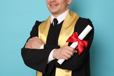 Photo of Happy student with diploma after graduation on light blue background, closeup