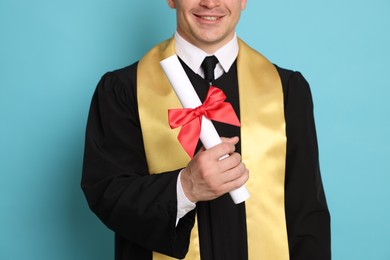Photo of Happy student with diploma after graduation on light blue background, closeup