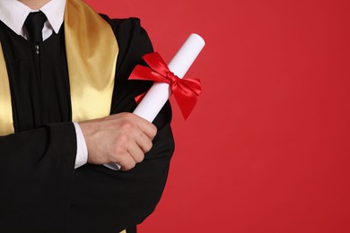 Photo of Student with diploma after graduation on red background, closeup. Space for text