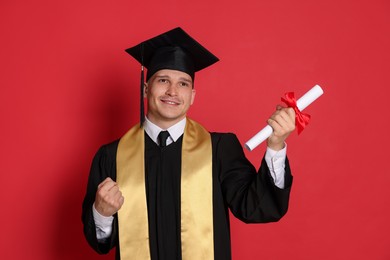 Photo of Happy student with diploma after graduation on red background