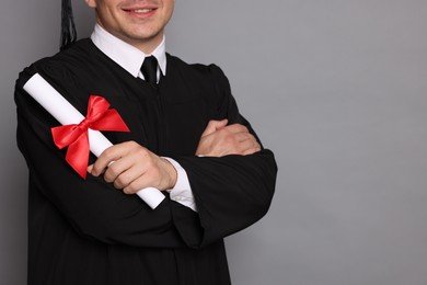 Photo of Happy student with diploma after graduation on grey background, closeup. Space for text