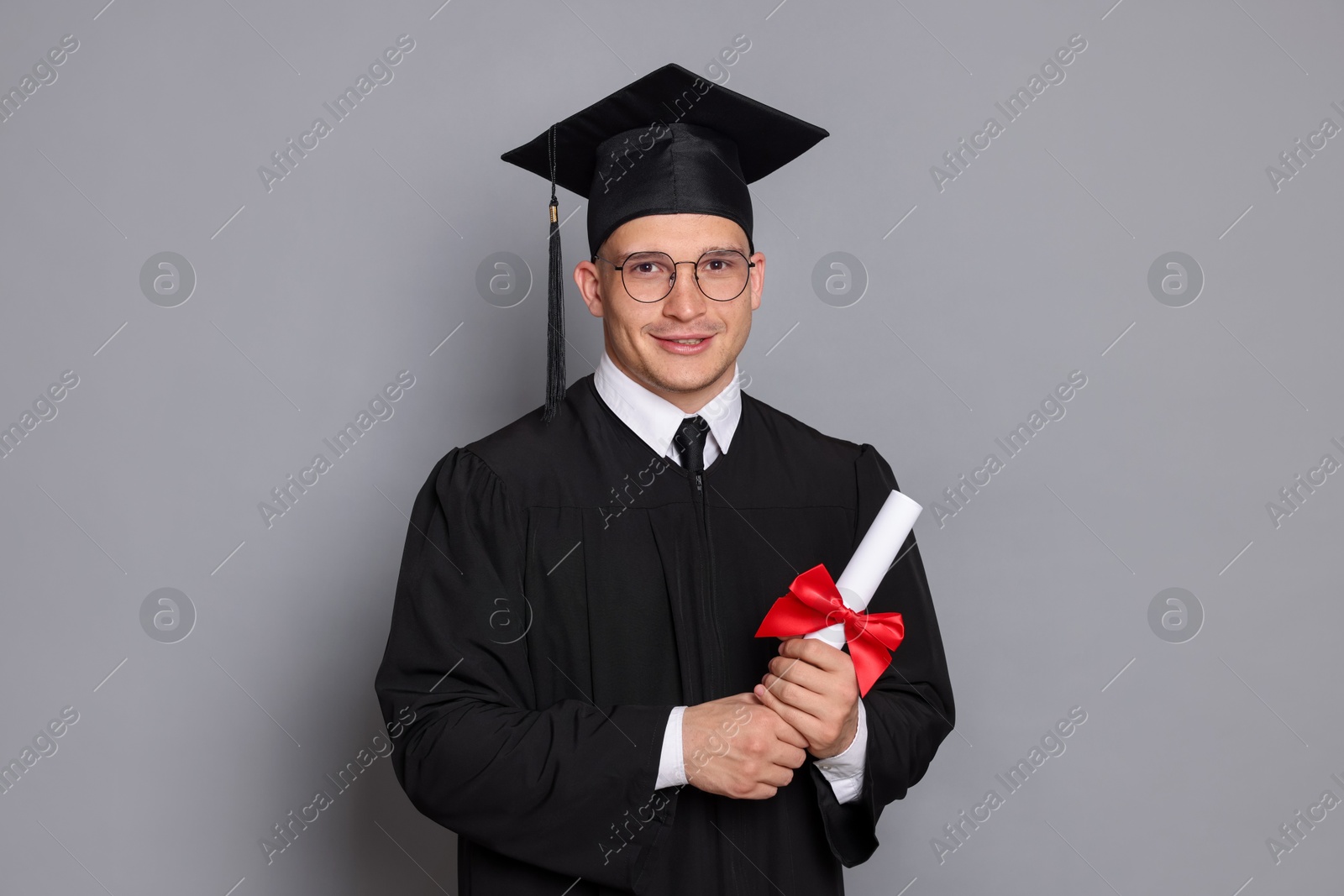 Happy student with diploma after graduation on grey background Photo of Happy student with diploma after graduation on grey background