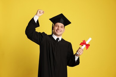Photo of Happy student with diploma after graduation on yellow background