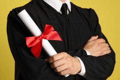 Photo of Student with diploma after graduation on yellow background, closeup