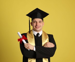 Photo of Happy student with diploma after graduation on yellow background