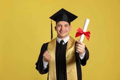 Photo of Happy student with diploma after graduation on yellow background