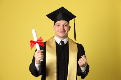 Photo of Happy student with diploma after graduation on yellow background