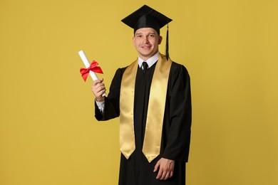 Photo of Happy student with diploma after graduation on yellow background