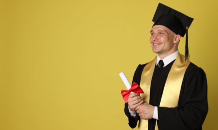 Photo of Happy student with diploma after graduation on yellow background. Space for text