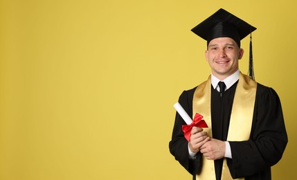 Photo of Happy student with diploma after graduation on yellow background. Space for text