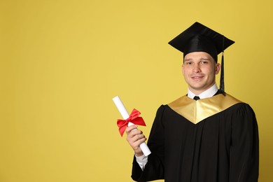 Photo of Happy student with diploma after graduation on yellow background. Space for text