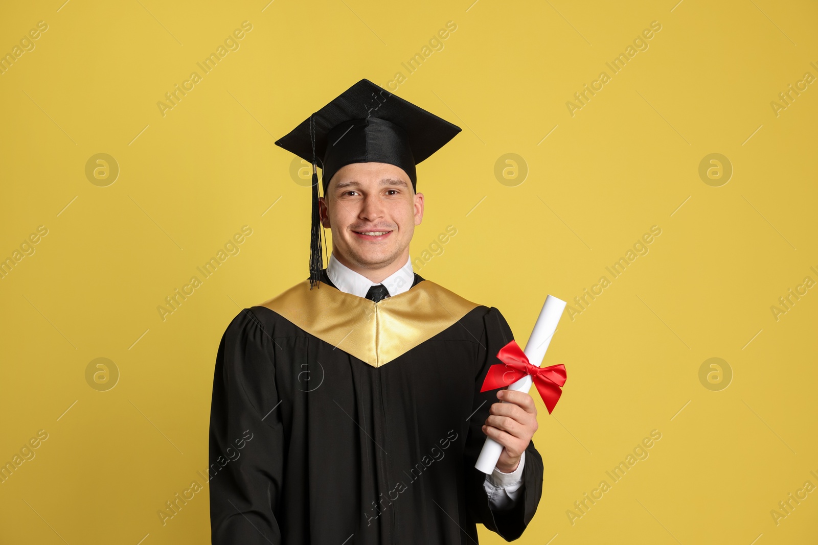 Happy student with diploma after graduation on yellow background Photo of Happy student with diploma after graduation on yellow background