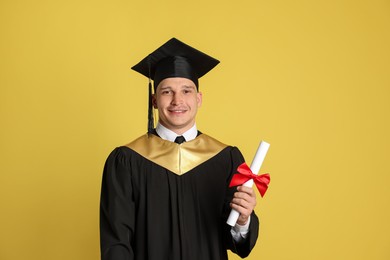 Photo of Happy student with diploma after graduation on yellow background