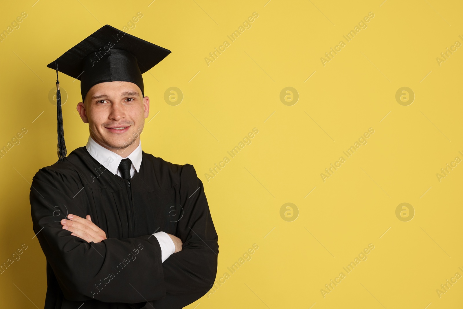 Happy student with crossed arms after graduation on yellow background. Space for text Photo of Happy student with crossed arms after graduation on yellow background. Space for text