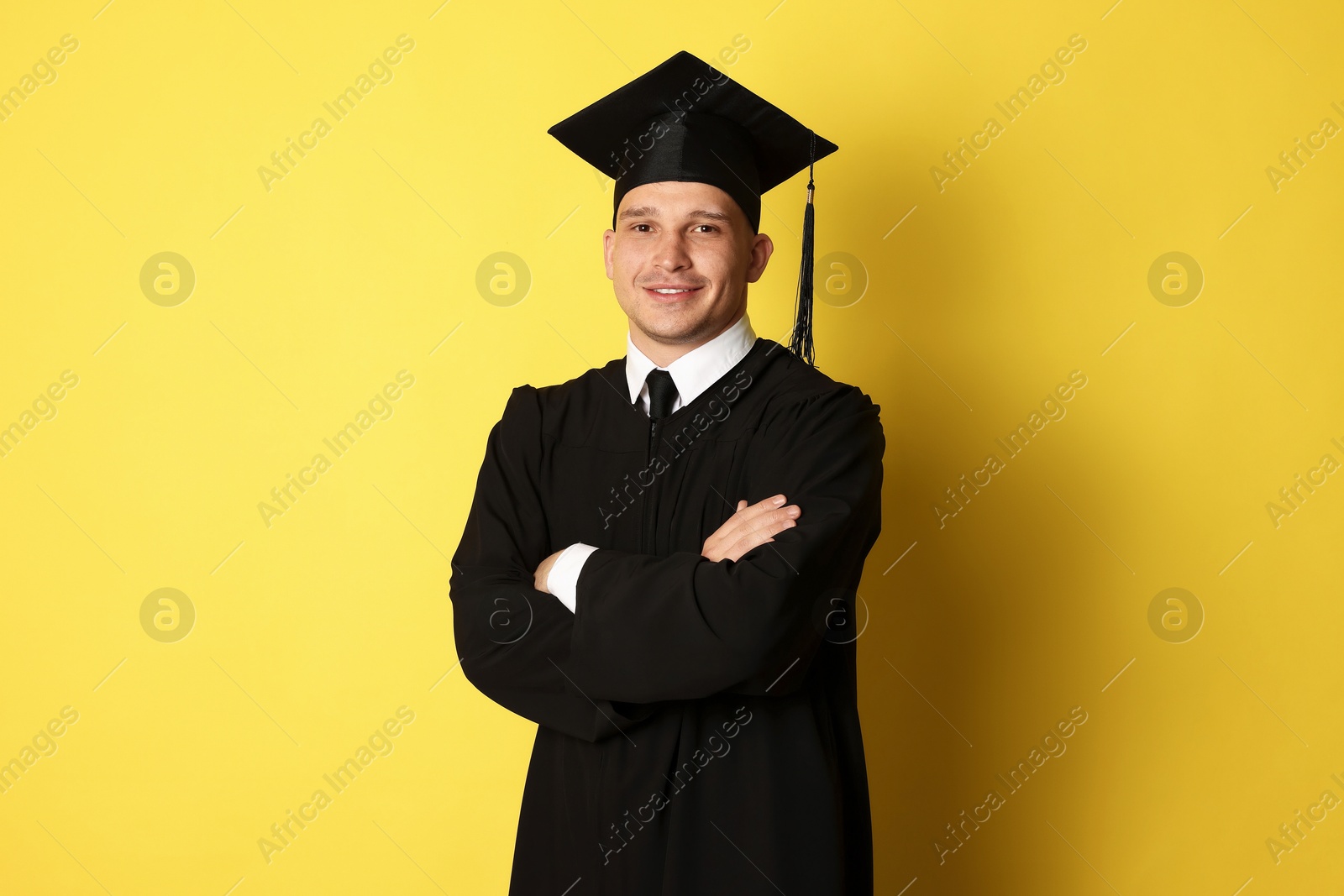Happy student with crossed arms after graduation on yellow background Photo of Happy student with crossed arms after graduation on yellow background