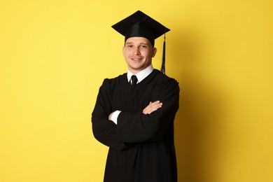 Photo of Happy student with crossed arms after graduation on yellow background