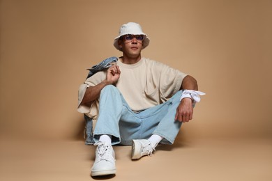 Photo of Fashionable portrait of handsome man in stylish outfit on brown background