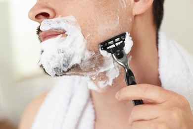 Photo of Man shaving with razor at home, closeup