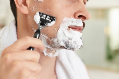 Photo of Man shaving with razor at home, closeup