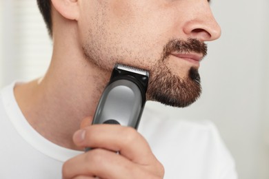 Photo of Man shaving with trimmer at home, closeup