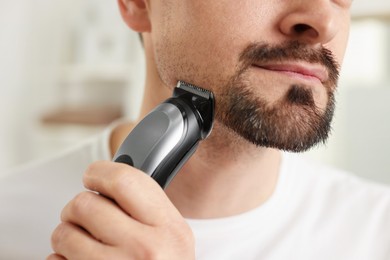 Photo of Man shaving with trimmer at home, closeup