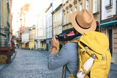Image of Tourist with backpack taking photo on city street, back view. Space for text