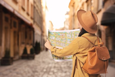 Image of Tourist with map and backpack on city street, back view. Space for text