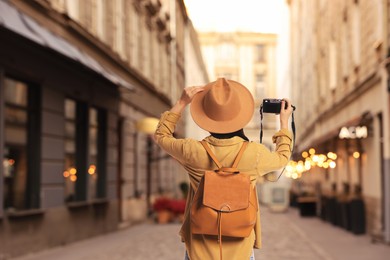 Image of Tourist with backpack taking photo on city street, back view