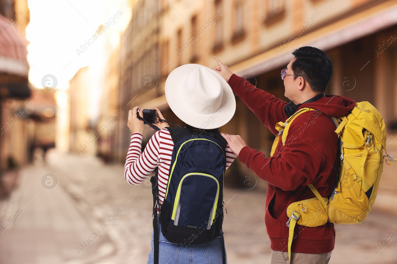 Tourists with backpacks taking photo on city street, back view Image of Tourists with backpacks taking photo on city street, back view