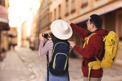 Image of Tourists with backpacks taking photo on city street, back view