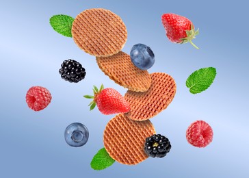 Image of Tasty Dutch waffles, fresh berries and mint flying on blue gradient background
