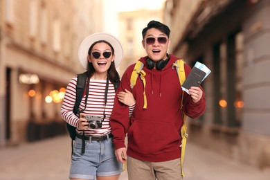 Image of Happy tourists with backpacks, flight tickets and camera on city street