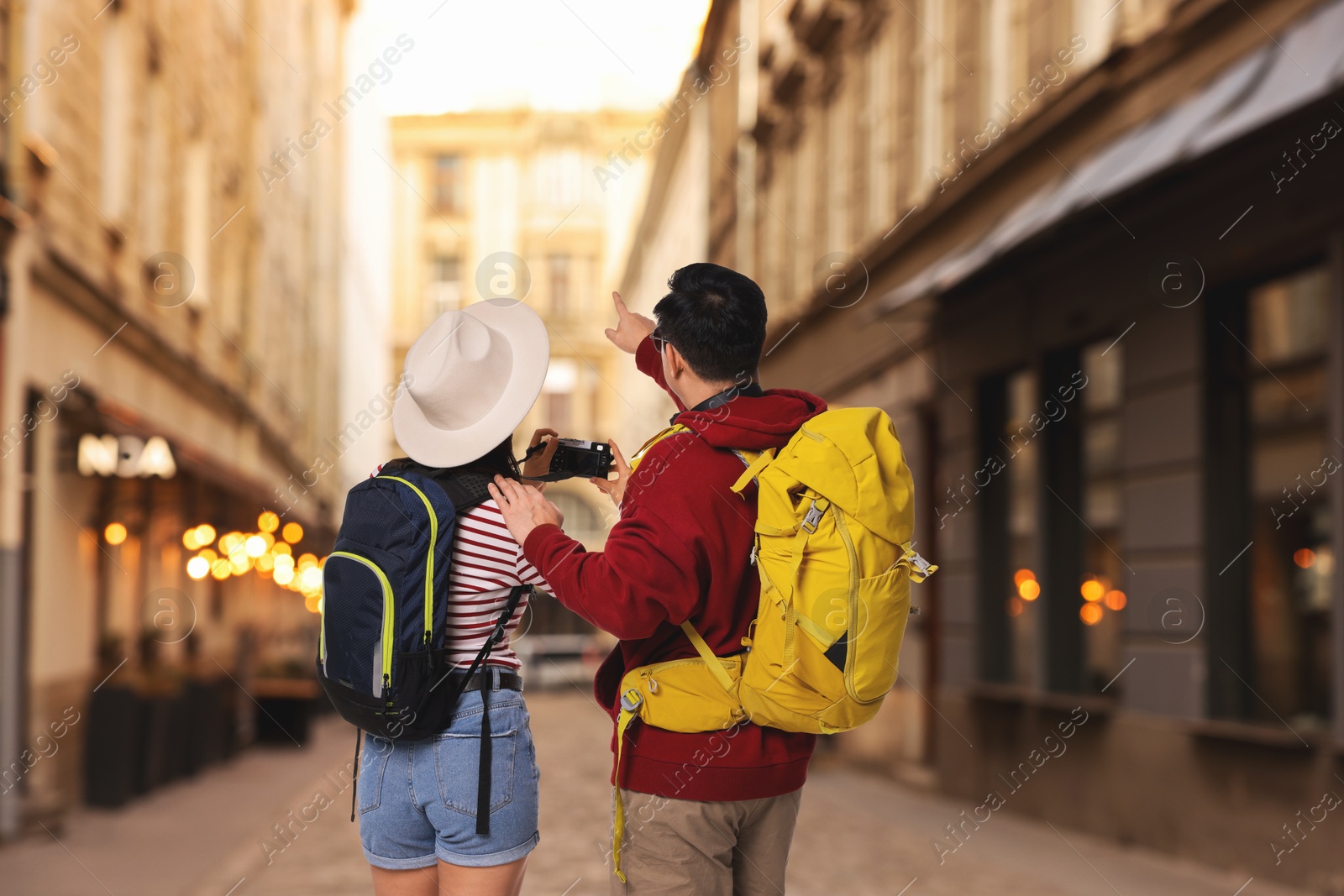Tourists with backpacks taking photo on city street, back view Image of Tourists with backpacks taking photo on city street, back view