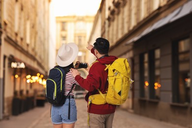 Image of Tourists with backpacks taking photo on city street, back view