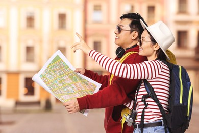 Image of Happy tourists with map pointing at something on city street