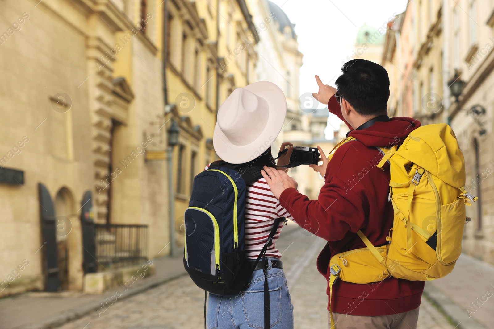 Tourists with backpacks taking photo on city street, back view. Space for text Image of Tourists with backpacks taking photo on city street, back view. Space for text