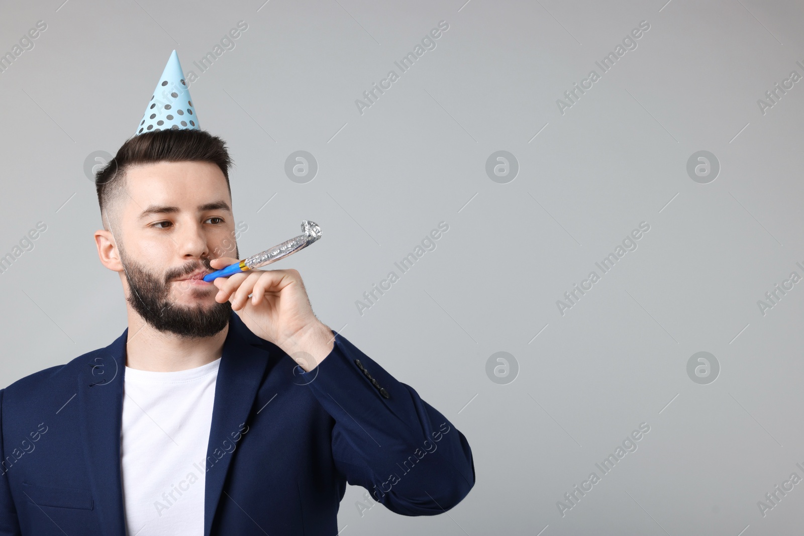 Happy Birthday. Handsome man with party hat and blower on grey background, space for text Photo of Happy Birthday. Handsome man with party hat and blower on grey background, space for text