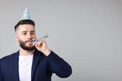 Photo of Happy Birthday. Handsome man with party hat and blower on grey background, space for text