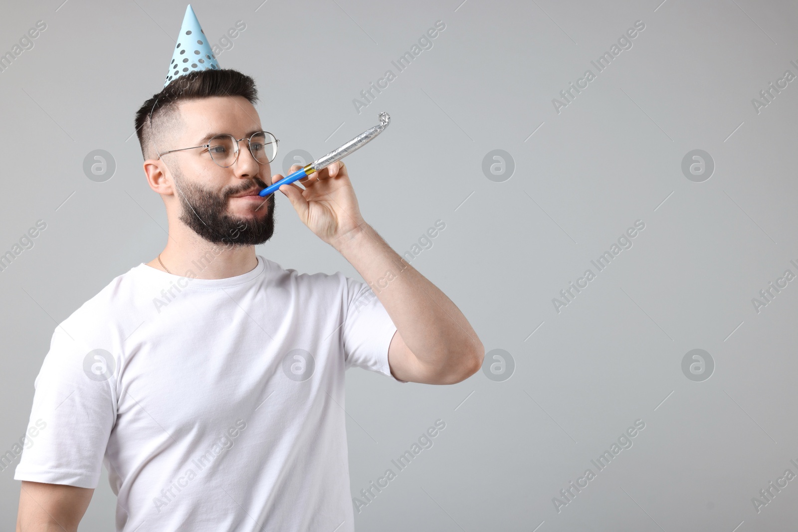 Happy Birthday. Handsome man with party hat and blower on grey background, space for text Photo of Happy Birthday. Handsome man with party hat and blower on grey background, space for text