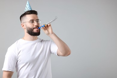 Photo of Happy Birthday. Handsome man with party hat and blower on grey background, space for text